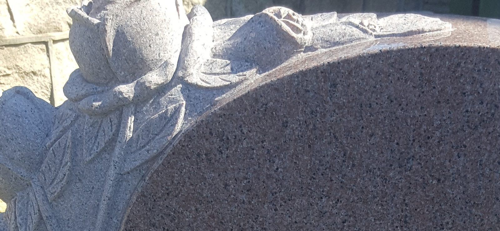 A rose and leaves carved in relief along the shaped crown of a mauve granite monument