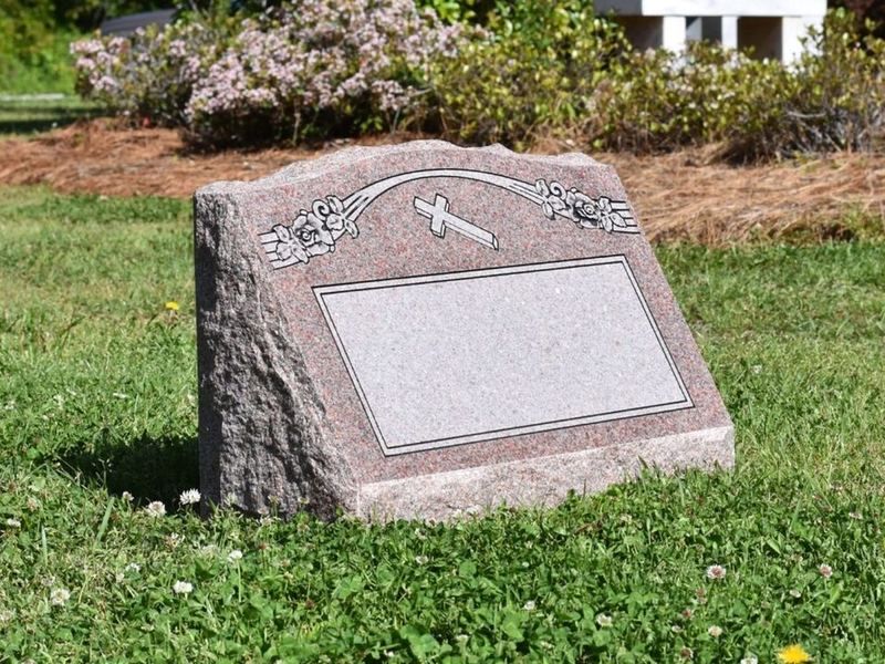 A Morning Rose granite slant headstone with a carved cross and roses above a blank panel