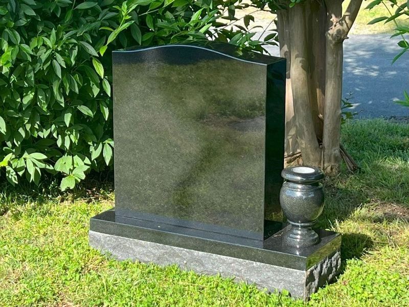 A polished Jet Black upright headstone with a matching granite vase on its base, standing on a lawn