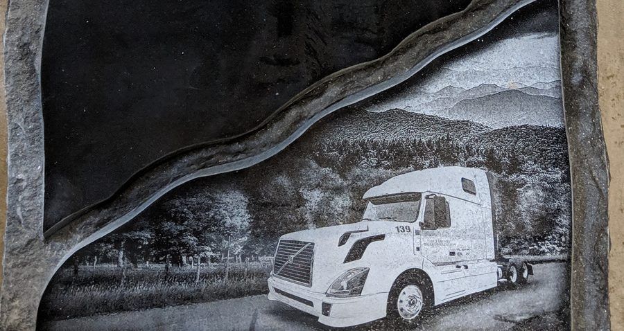 A hand etched truck scene on the face of a black granite upright monument, photographed in the Winnsboro shop