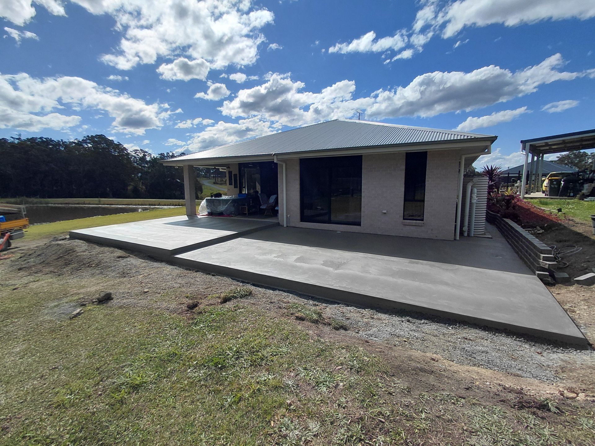 Partially Built White House with A Concrete Driveway Under a Cloudy Blue Sky — Kempsey Concrete Contractors PTY LTD In Dondingalong, NSW