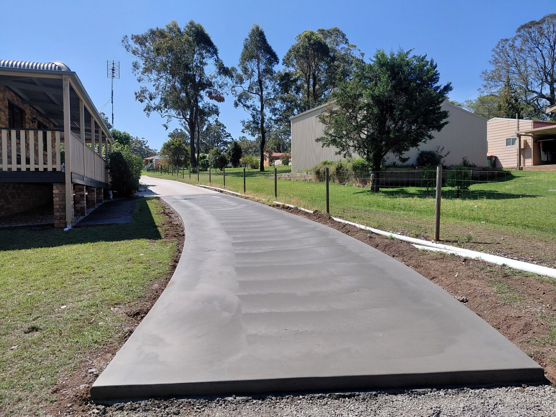 New Concrete Sidewalk Curving Through a Grassy Residential Area with Houses and Trees — Kempsey Concrete Contractors PTY LTD In South West Rocks, NSW