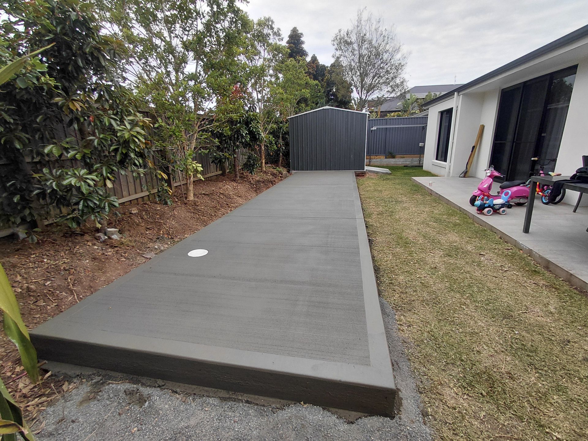 Concrete Backyard Path Beside a House, Ending at A Gray Shed, with Grass — Kempsey Concrete Contractors PTY LTD In Crescent Head, NSW