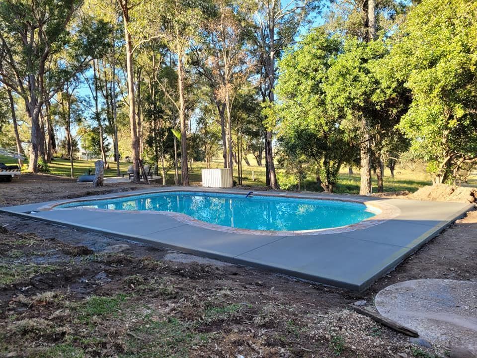 Outdoor Swimming Pool with A Blue Surface, Surrounded by Concrete and Trees in A Wooded Area — Kempsey Concrete Contractors PTY LTD In Dondingalong, NSW