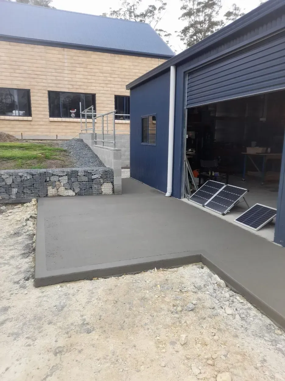 Blue Garage with Concrete Ramp and Gravel Driveway Beside a Beige Building Outdoors — Kempsey Concrete Contractors PTY LTD In Dondingalong, NSW