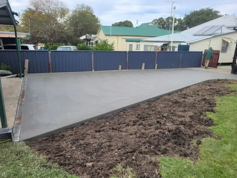 Freshly Poured Concrete Slab Beside a Dirt Strip in A Backyard with A Blue Fence — Kempsey Concrete Contractors PTY LTD In Dondingalong, NSW