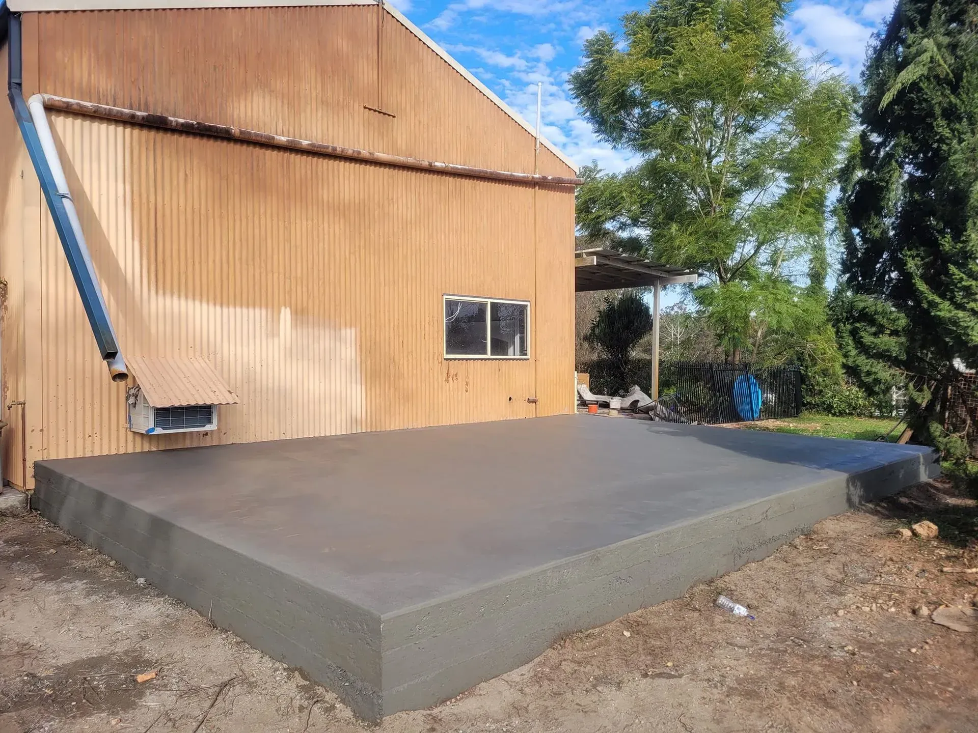 Concrete Slab Foundation Beside a Wooden Building Under Construction — Kempsey Concrete Contractors PTY LTD In Dondingalong, NSW
