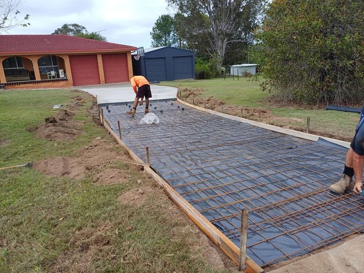 Workers pour concrete for a driveway beside a house, with steel rebar laid out on the slab.