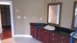 Bathroom vanity with dark wood cabinets, black countertop, and wall mirror beside an open doorway