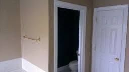 Bathroom doorway with white door, beige walls, and a towel bar on the left.