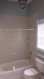 Small bathroom with white bathtub, toilet, tiled walls, and a window with blinds.