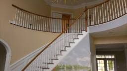Curved staircase in a beige foyer with white railings and a large arched doorway