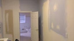 Empty room with beige walls, open door, and white trim leading to a bathroom or closet.