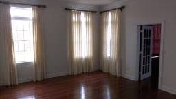 Empty living room with hardwood floors, cream curtains, and a windowed doorway on the right