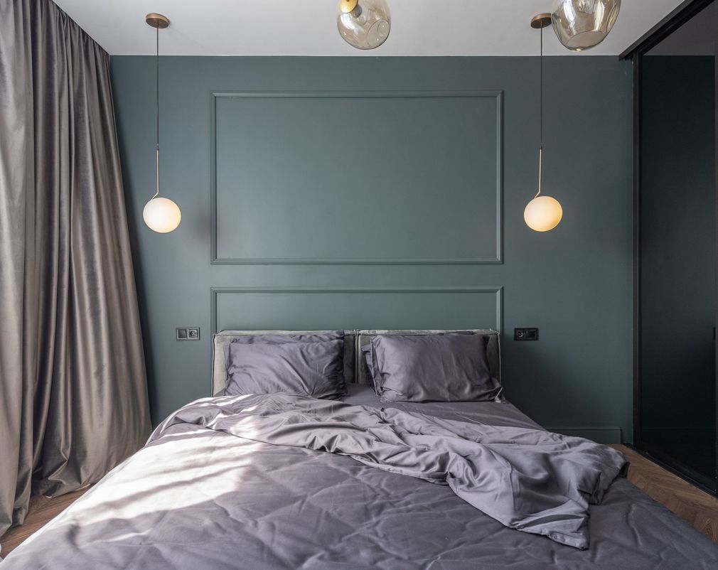 Modern bedroom with teal walls, gray bedding, pendant lights, and large curtains