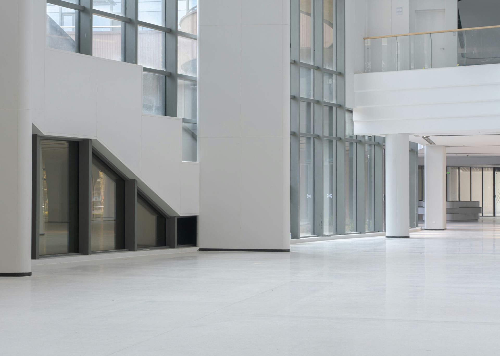 Bright modern atrium with tall glass windows, white walls, and a spacious empty floor