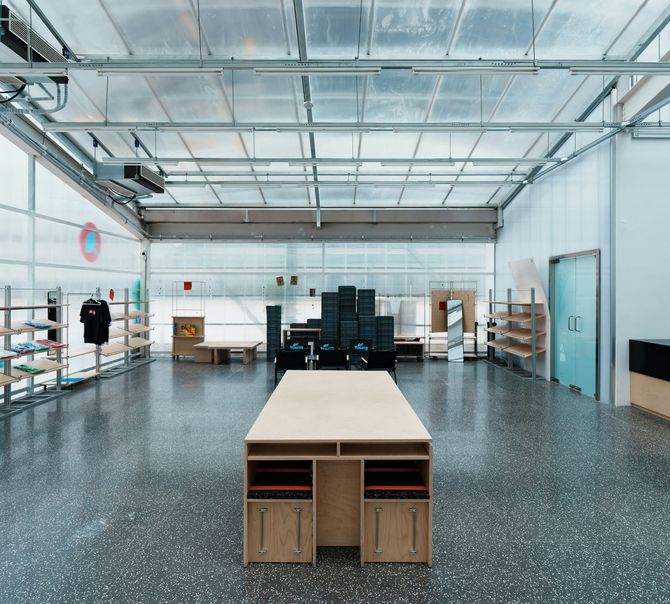 Spacious modern workshop with a large wooden table, shelving, and a black counter under a glass ceiling