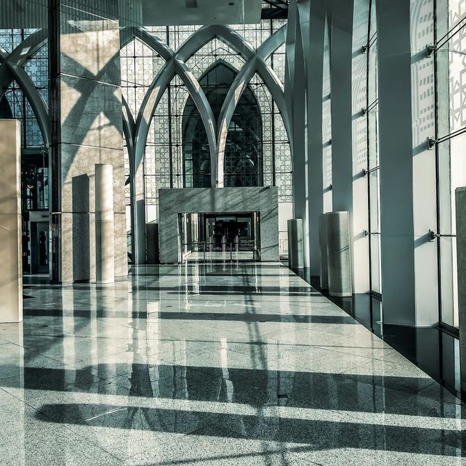 Sunlit modern glass atrium with arched columns and long floor shadows