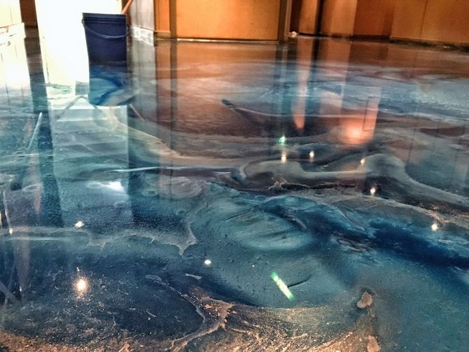 Blue reflective glass floor with swirling patterns and a bucket near a doorway