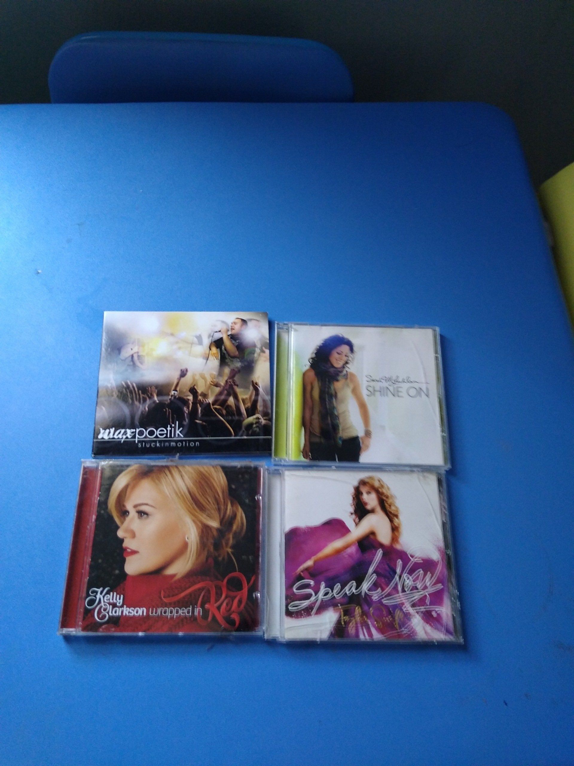 Four CDs on a blue surface:  alt-J album, an album with a person wearing a beige top, an album with a blonde woman