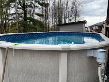 An oval above-ground swimming pool with light gray patterned siding and a white top rail, set in a backyard.