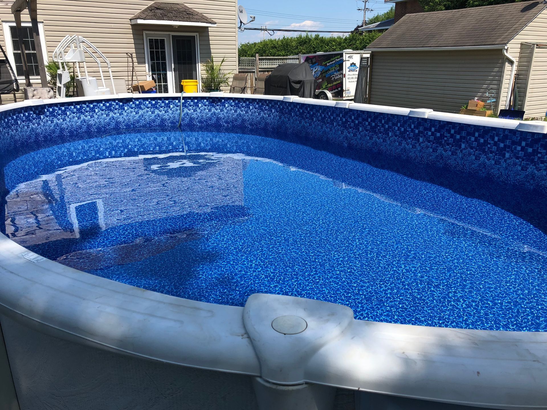 An above-ground oval swimming pool with blue mosaic tile liner in a residential backyard.
