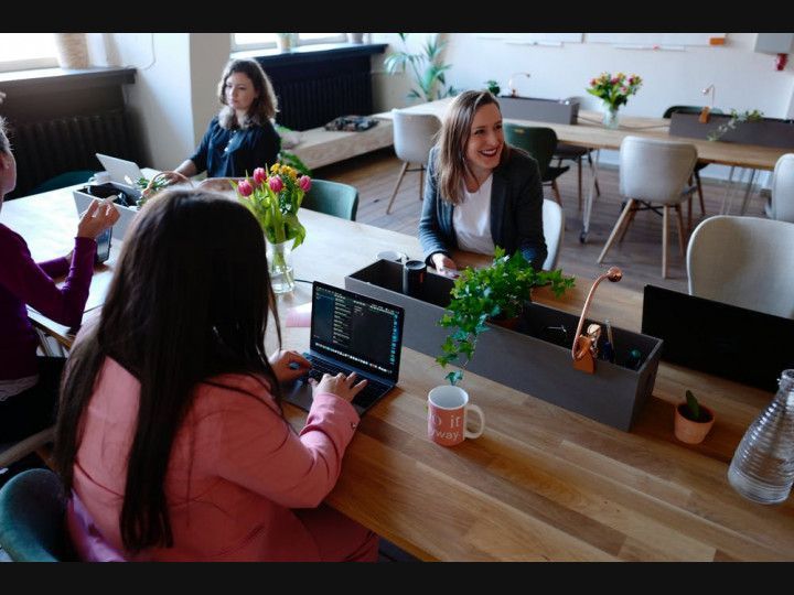 A group of women are sitting at a table with laptops .
