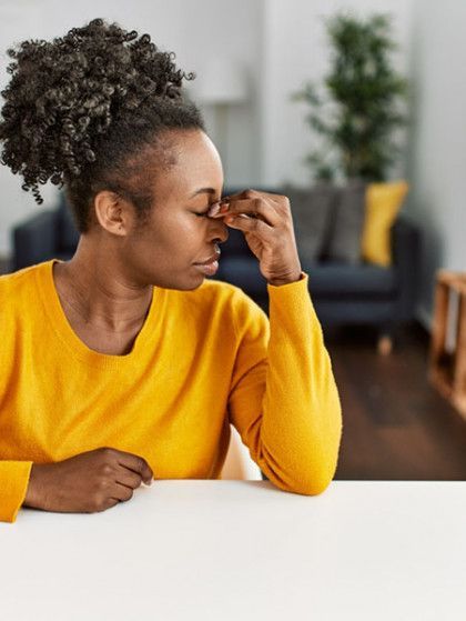A woman is sitting at a table with her hand on her nose .