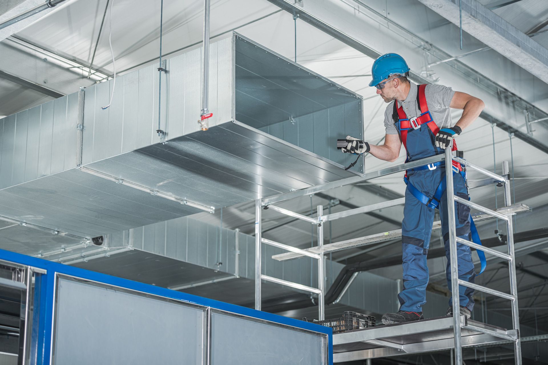 A man wearing a blue hard hat is working on a metal duct