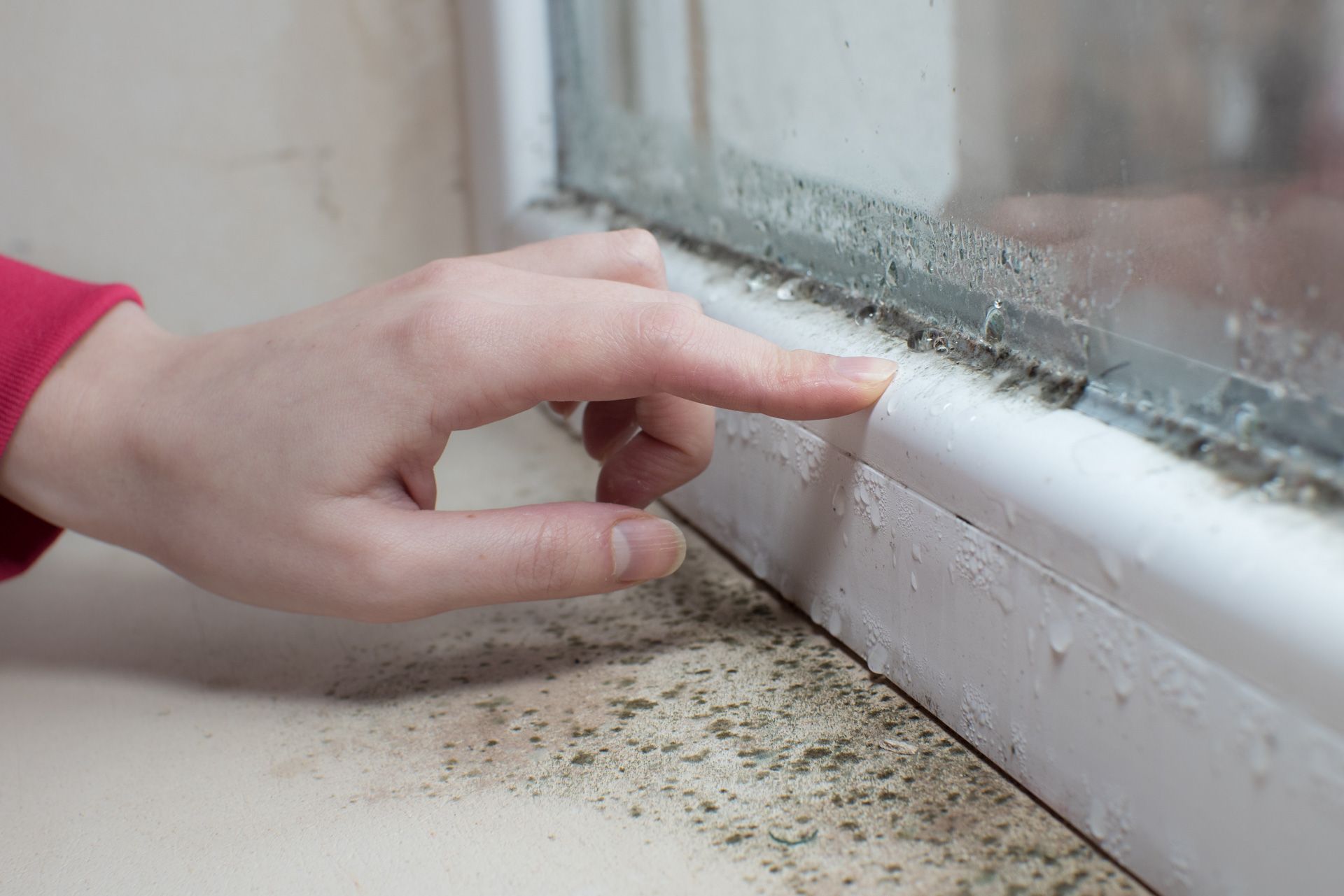 A person 's hand is pointing at a dirty window sill