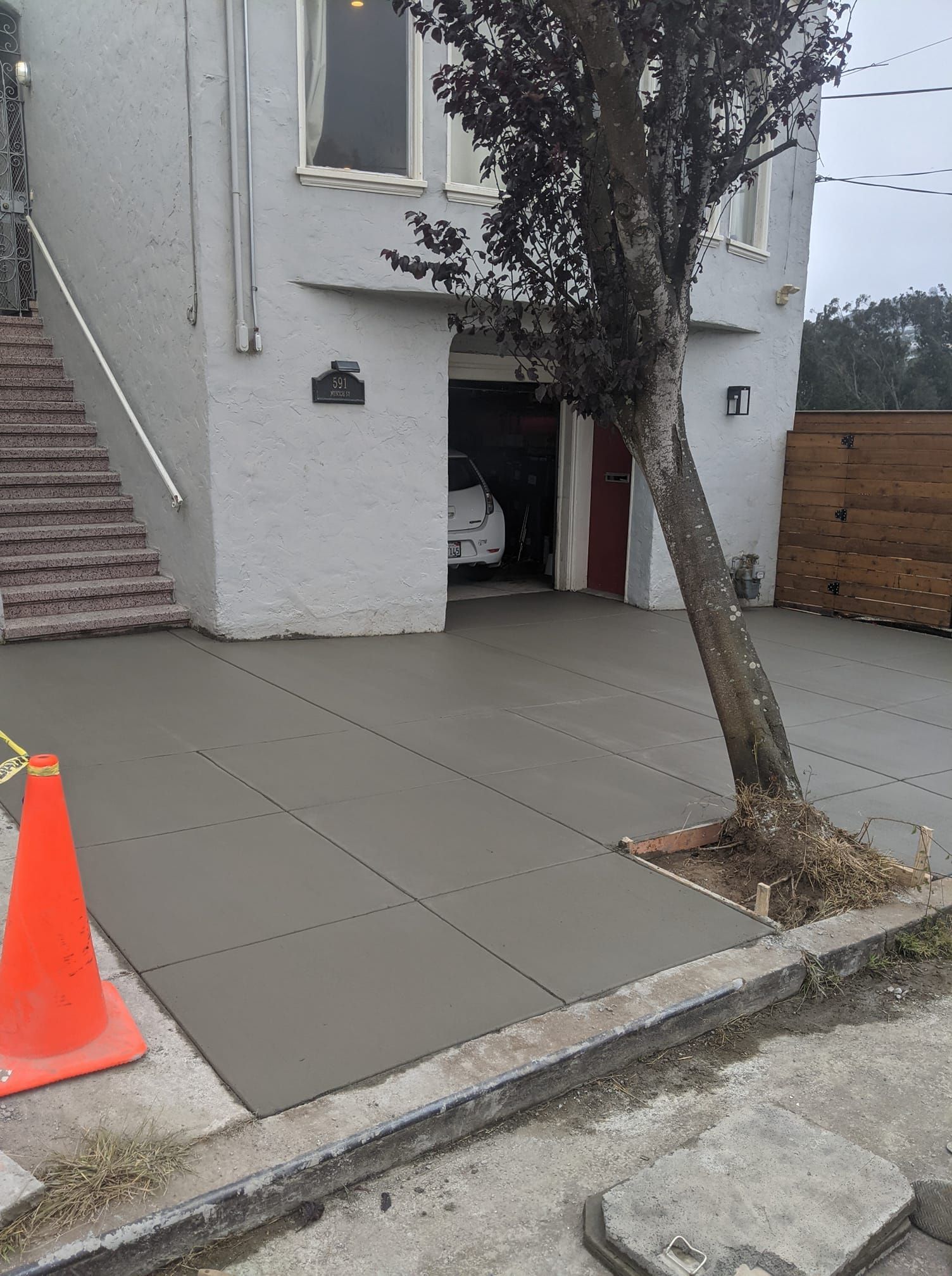 New concrete driveway in front of a light-colored building. An orange cone is on the left.