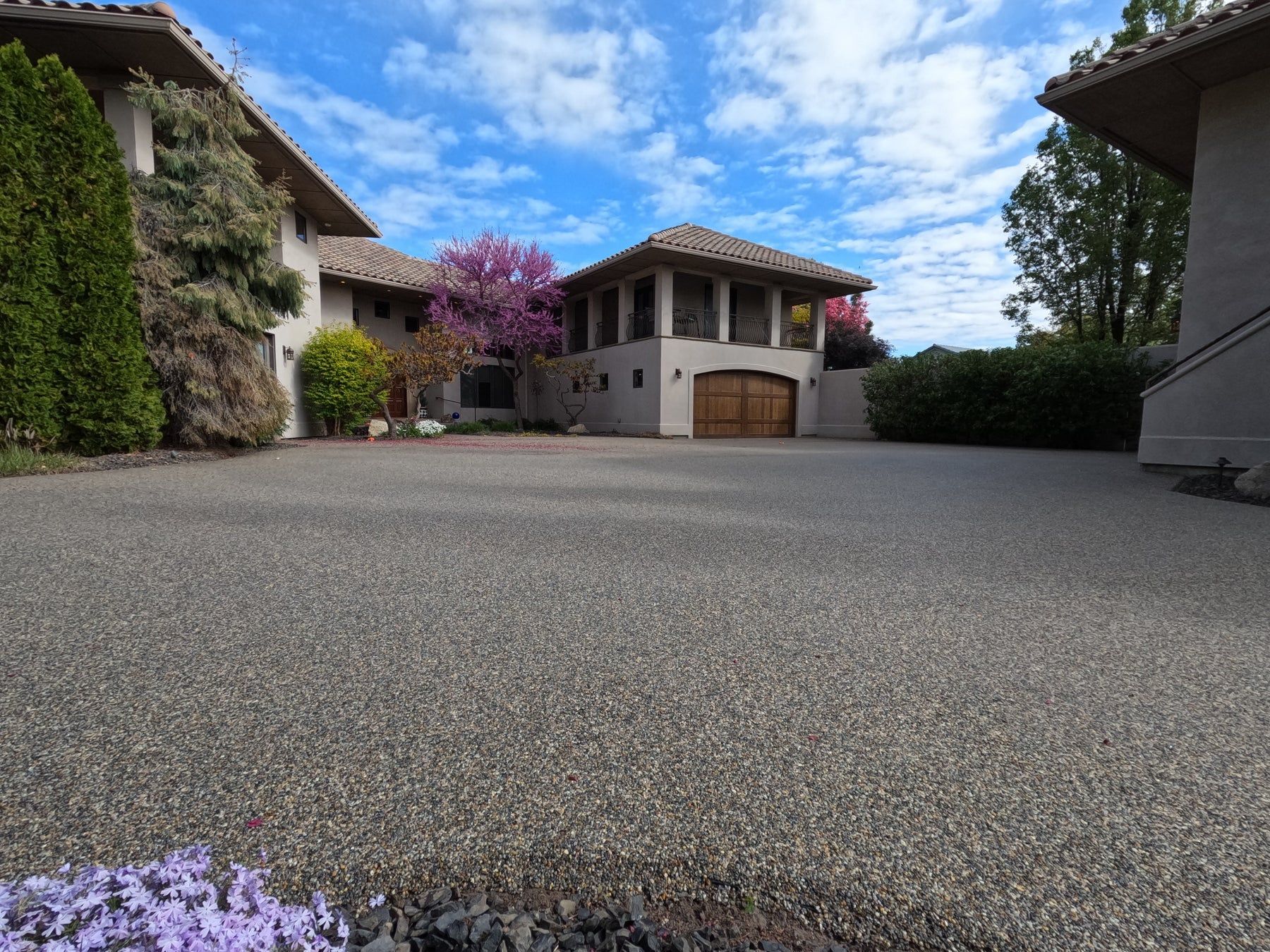 Gravel driveway leading to a multi-story home with a tan exterior, arched garage door, and blue sky.