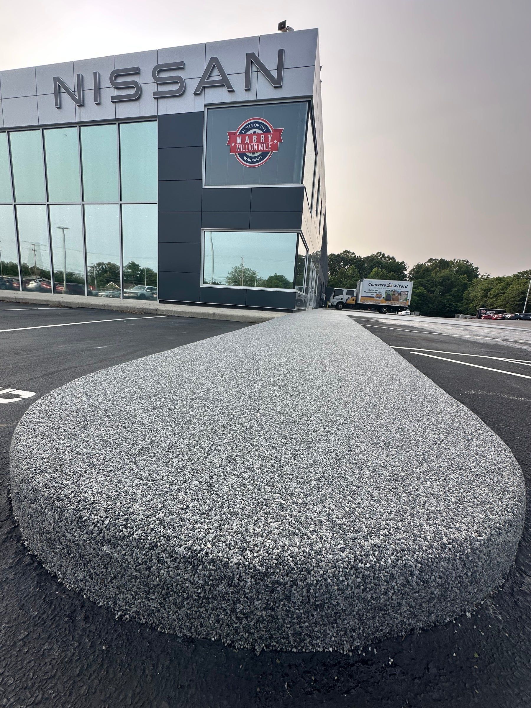 Nissan dealership building exterior with a gravel-covered landscaped area in front, set against an overcast sky.