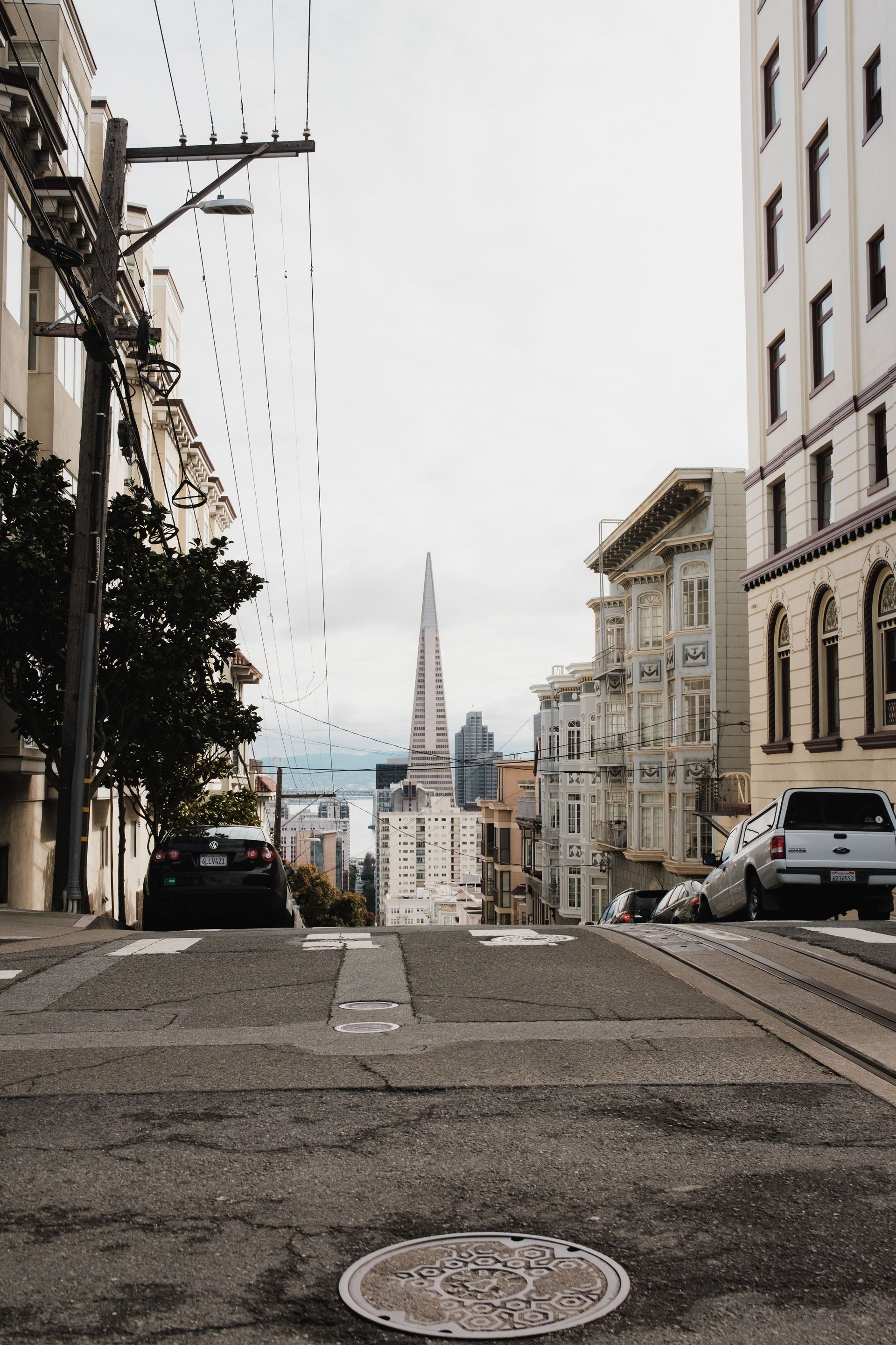 Steep city street overlooking a bay with a distant tower and buildings on both sides