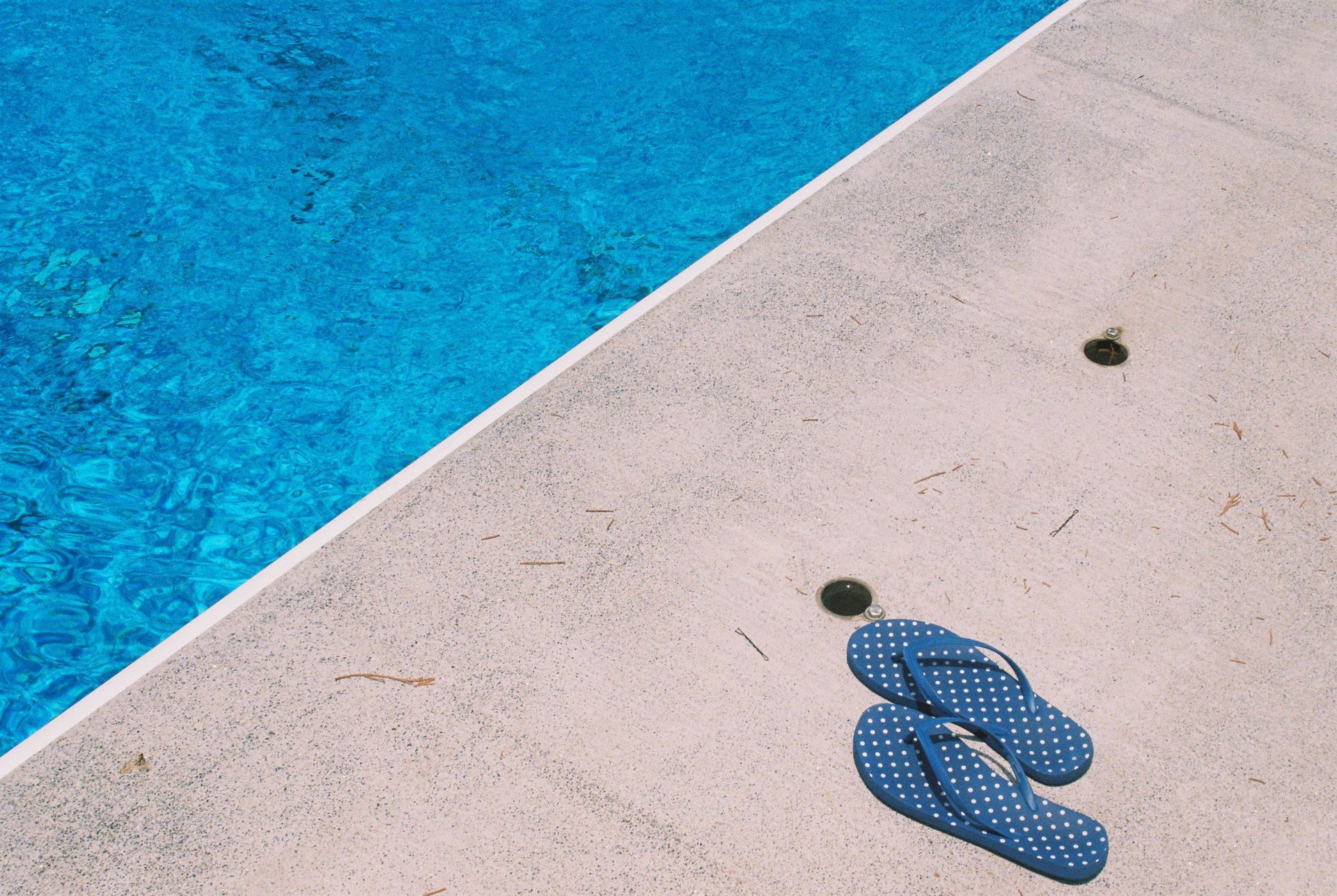 Blue flip-flops beside a turquoise pool on a light concrete deck