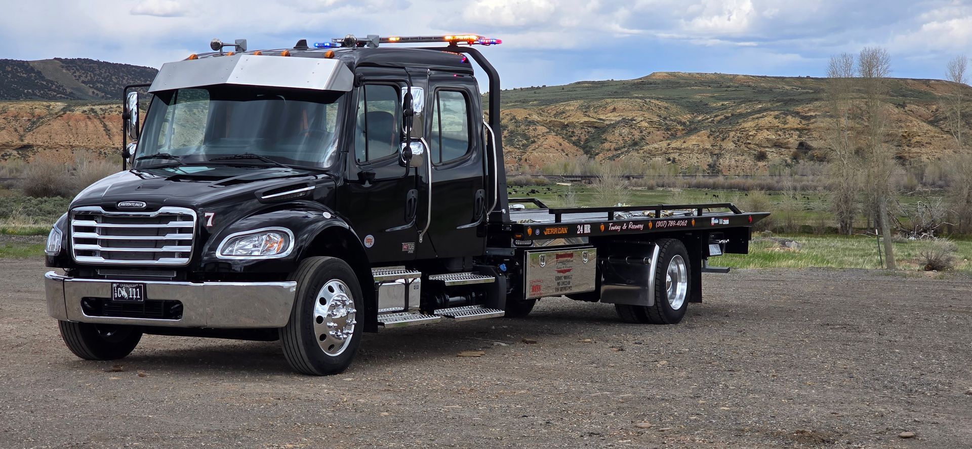 A purple tow truck is towing a black truck in a parking lot — Evanston, WY — Robertson Transportation Inc. Towing and Recovery