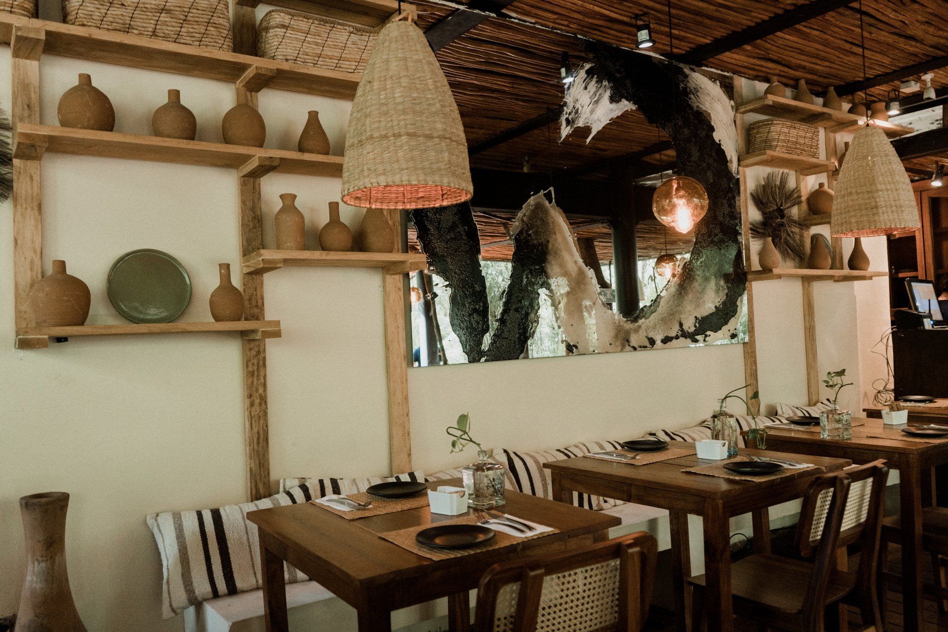 A restaurant with wooden tables and chairs and wicker lamps hanging from the ceiling.