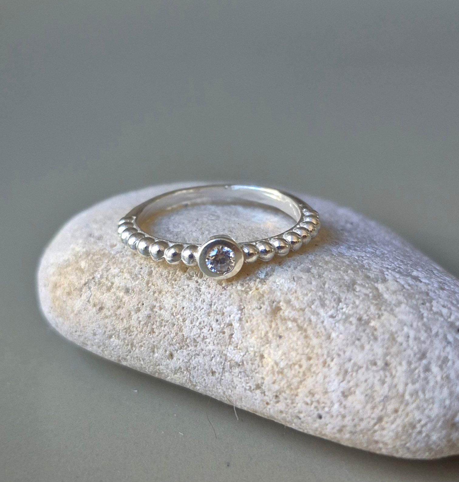 Anillo de plata con una pequeña piedra redonda y transparente sobre una piedra gris texturizada.