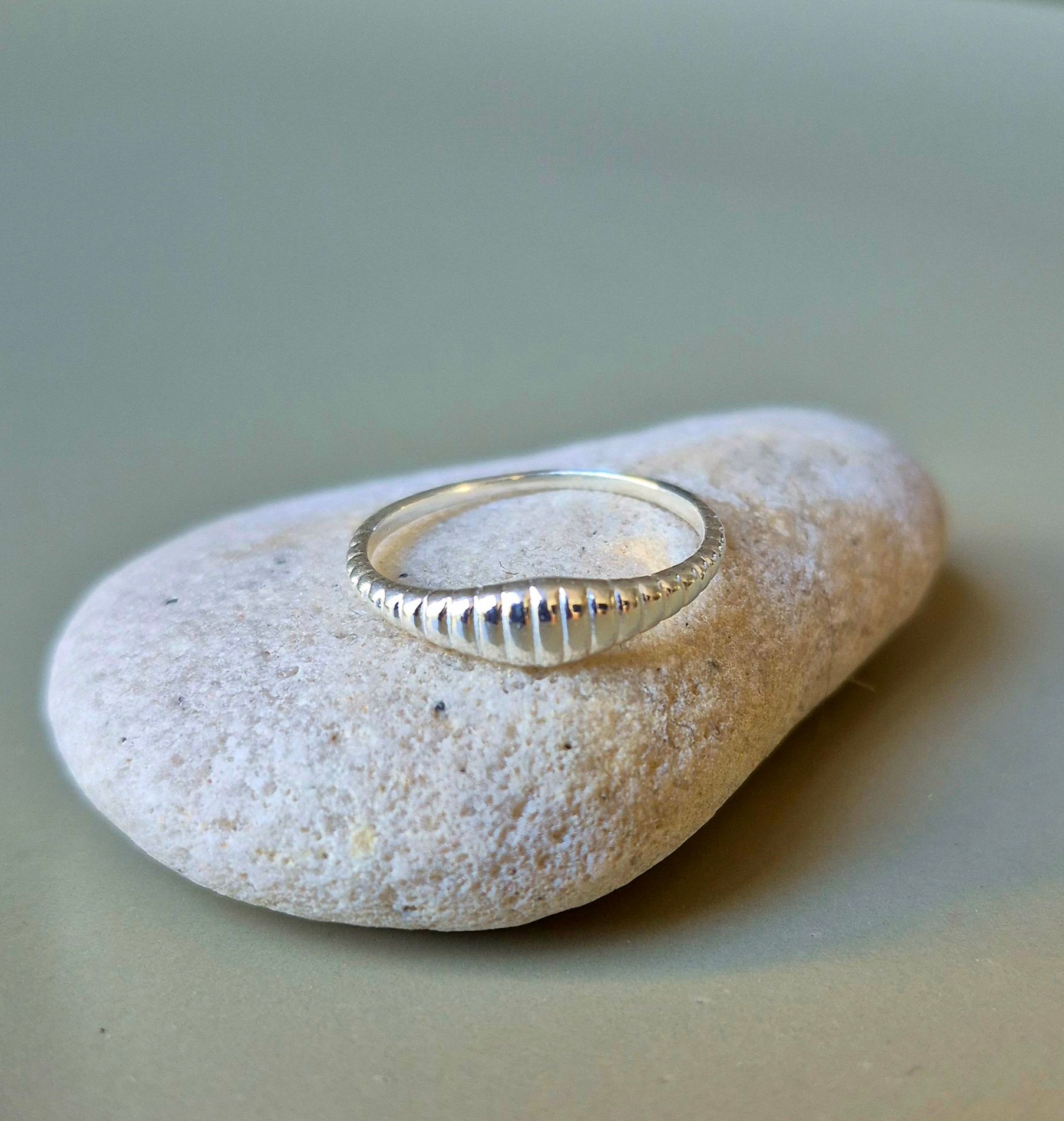 Anillo de plata con detalle estriado sobre una piedra blanca lisa.