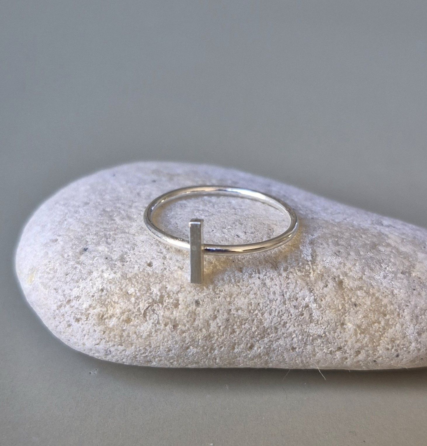 Anillo de plata con una barra vertical sobre una roca lisa y gris.