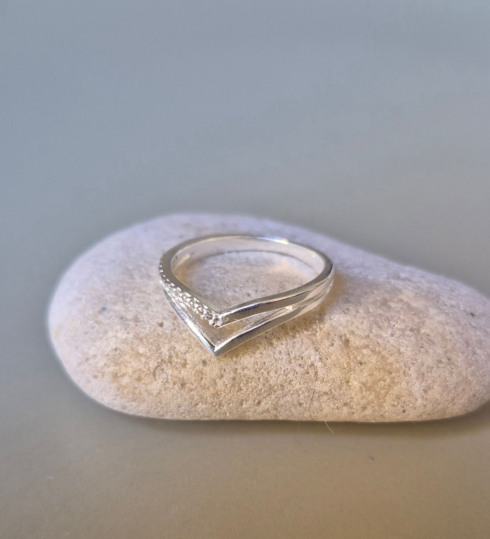 Anillo de plata con diseño de chevrón y pequeñas piedras sobre una piedra lisa gris.