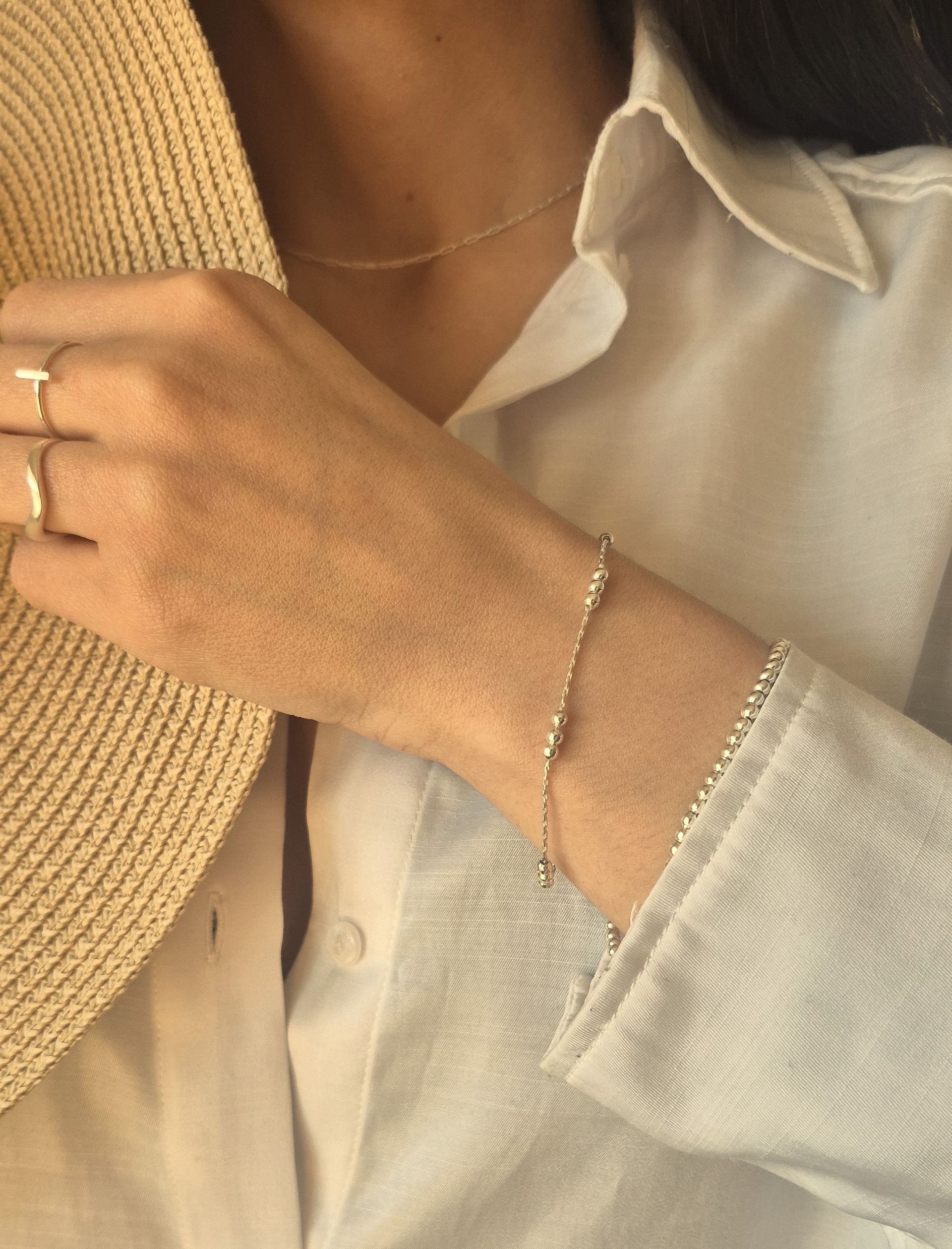 Mujer vestida con camisa blanca y joyas de oro, incluyendo collar, anillos y pulsera, sosteniendo un sombrero de paja.