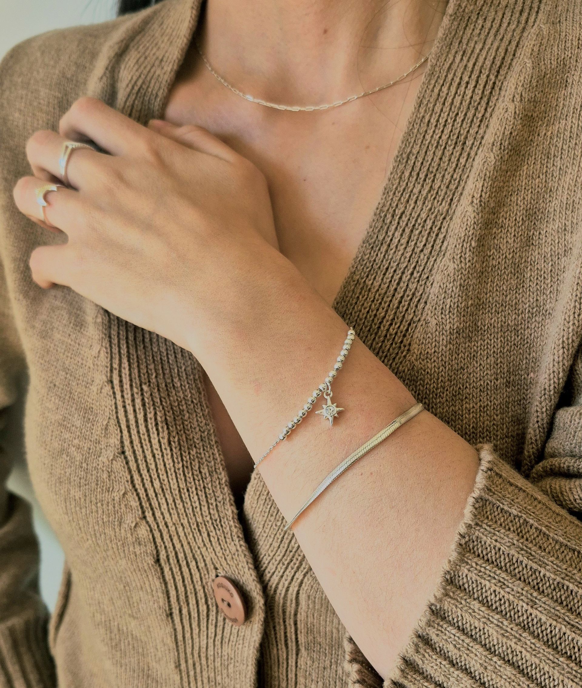 Mujer con cárdigan color canela y joyas de oro: collar, pulseras y anillos.