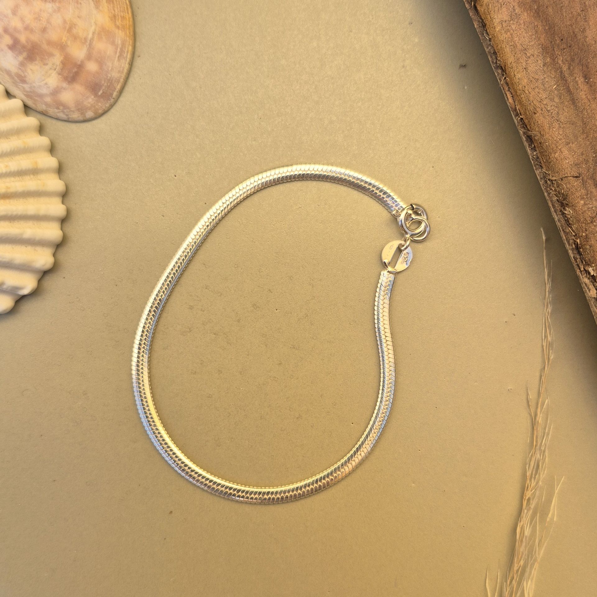 Pulsera de cadena plateada sobre una superficie neutra con adorno de concha y madera.