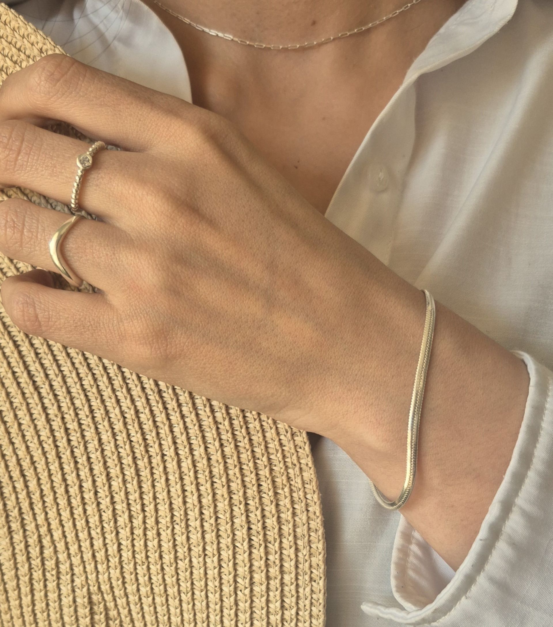 Persona que lleva joyas de plata: pulsera, anillos y collar, con camisa blanca y sombrero beige.