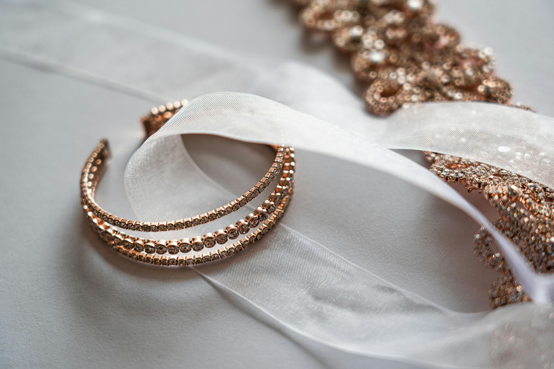 Pulseras de cuentas doradas y cinta sobre una suave superficie blanca; acento brillante en el fondo.