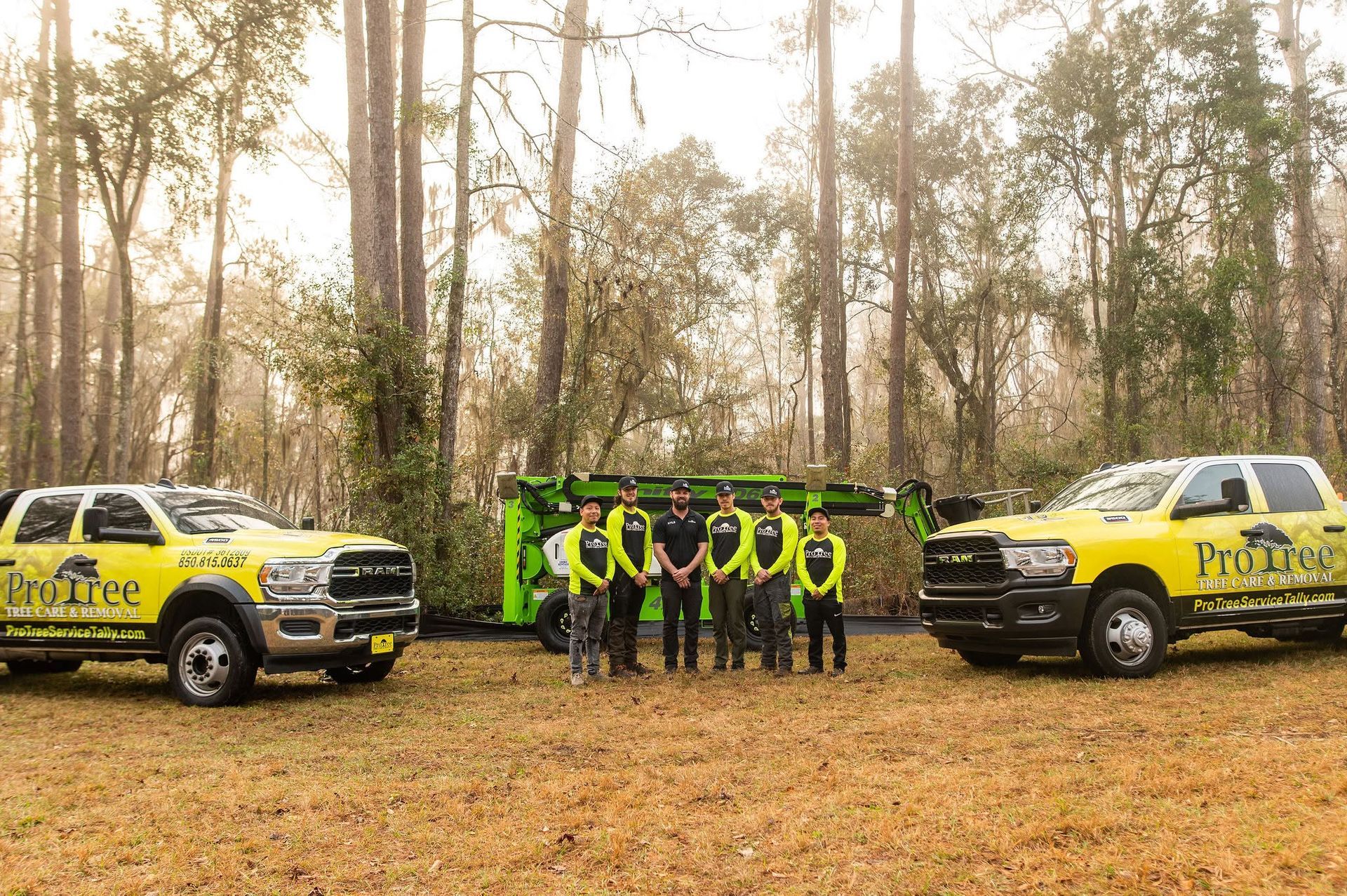 Trucks and crew in neon safety gear posing in a wooded clearing beside a trailer