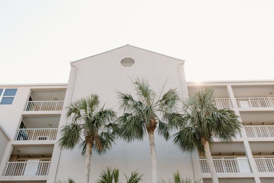 Low-rise apartment building with balconies and tall palm trees in front