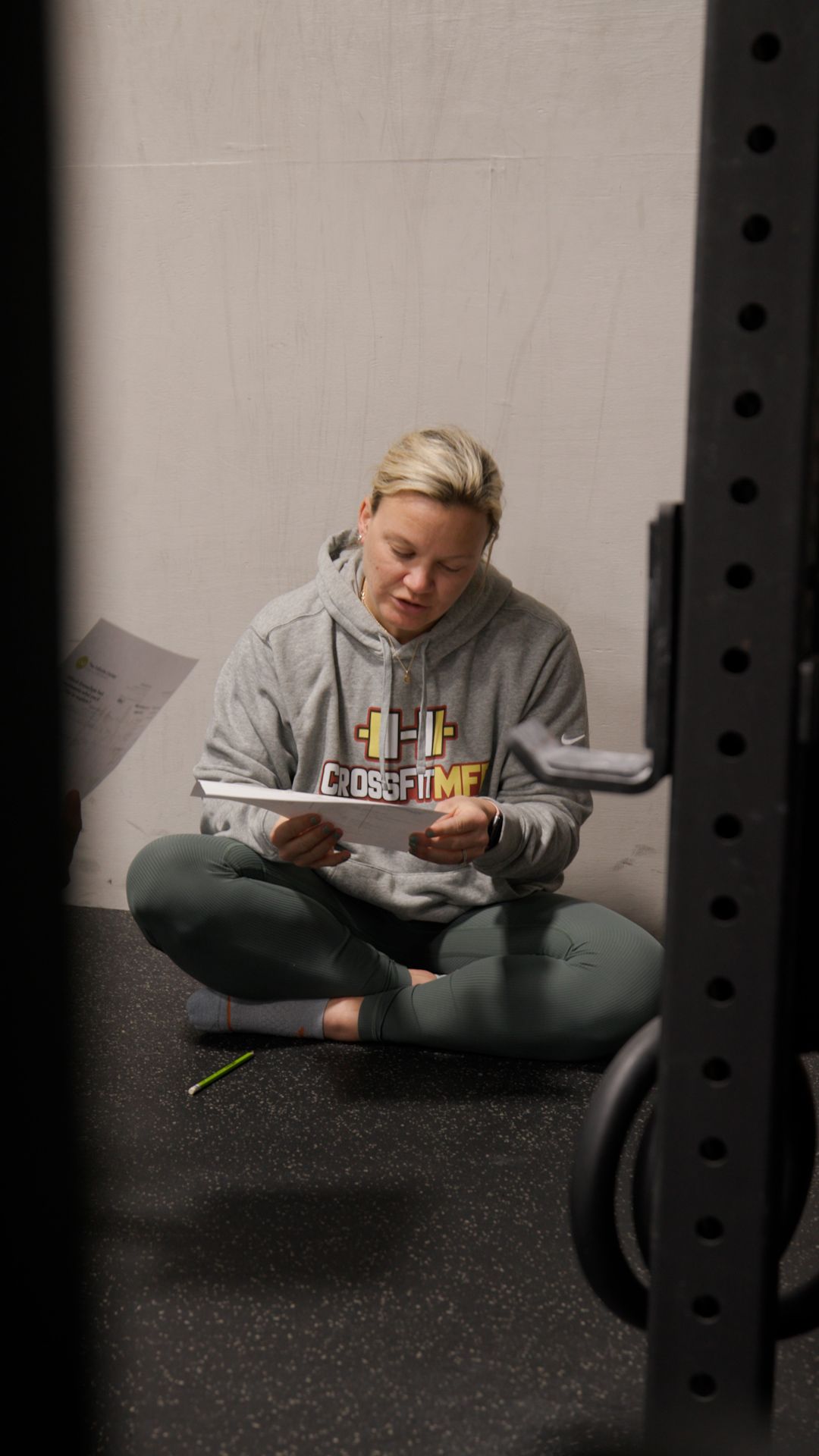 A woman is sitting on the floor reading a book in a gym.