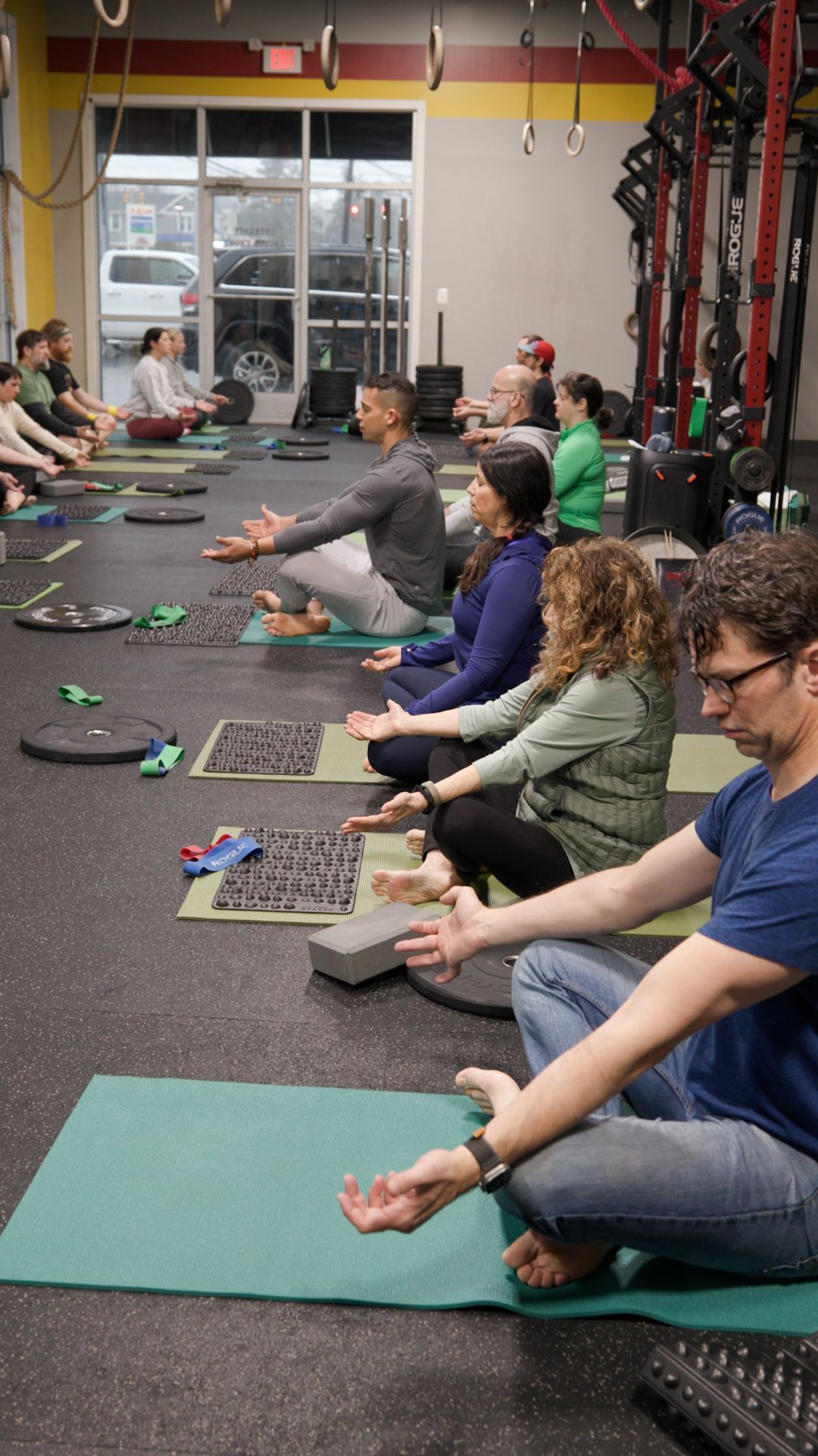 A group of people are sitting on yoga mats in a gym.